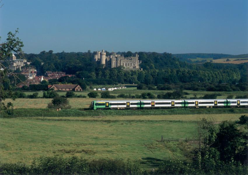 Train passing in front of stately castle peeking out from the surrounding tree tops-Arun Valley Line