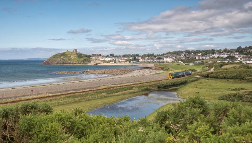 Train travelling along the coast with town and castle in background, Cambrian Coast, Wales on Rails