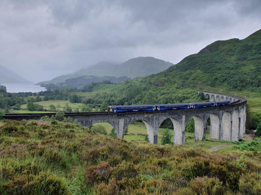 Train travelling along viaduct with green landscapes and mountains in the background | West Highland