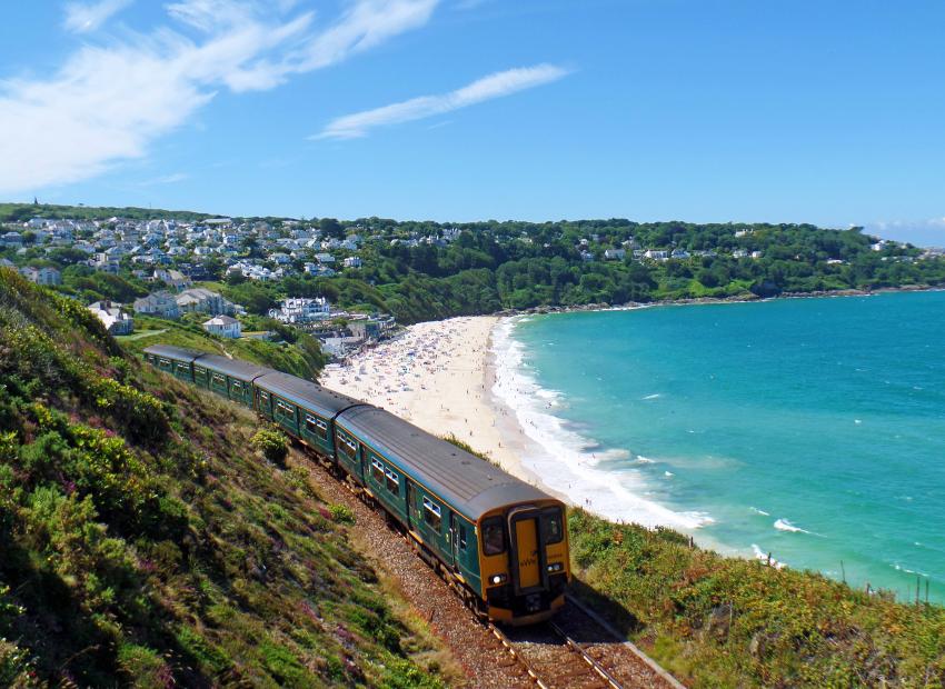 Train travelling past clear blue sea and village in background