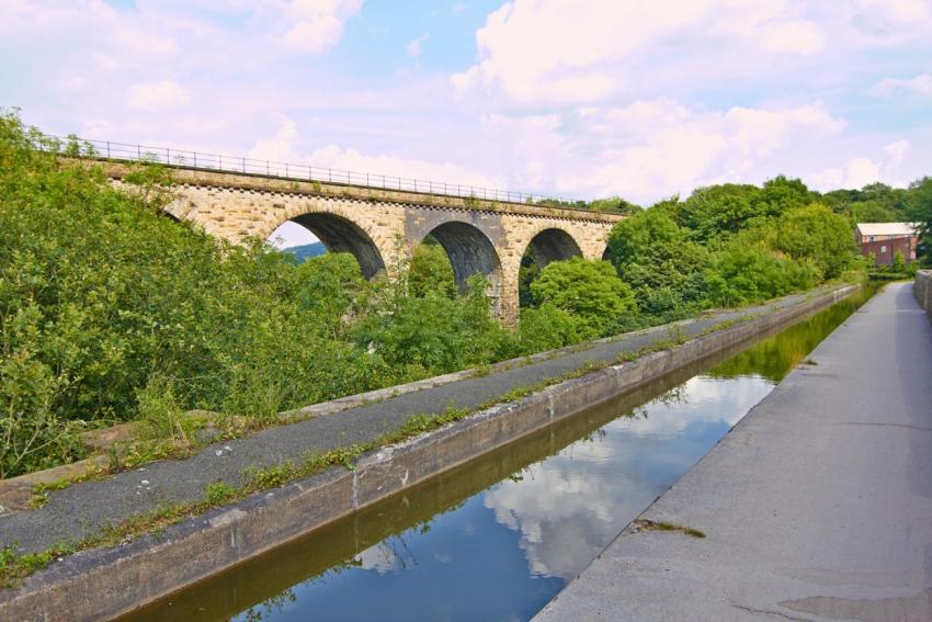 View of the top of an aquaduct with railway viaduct behind and lush greenery between