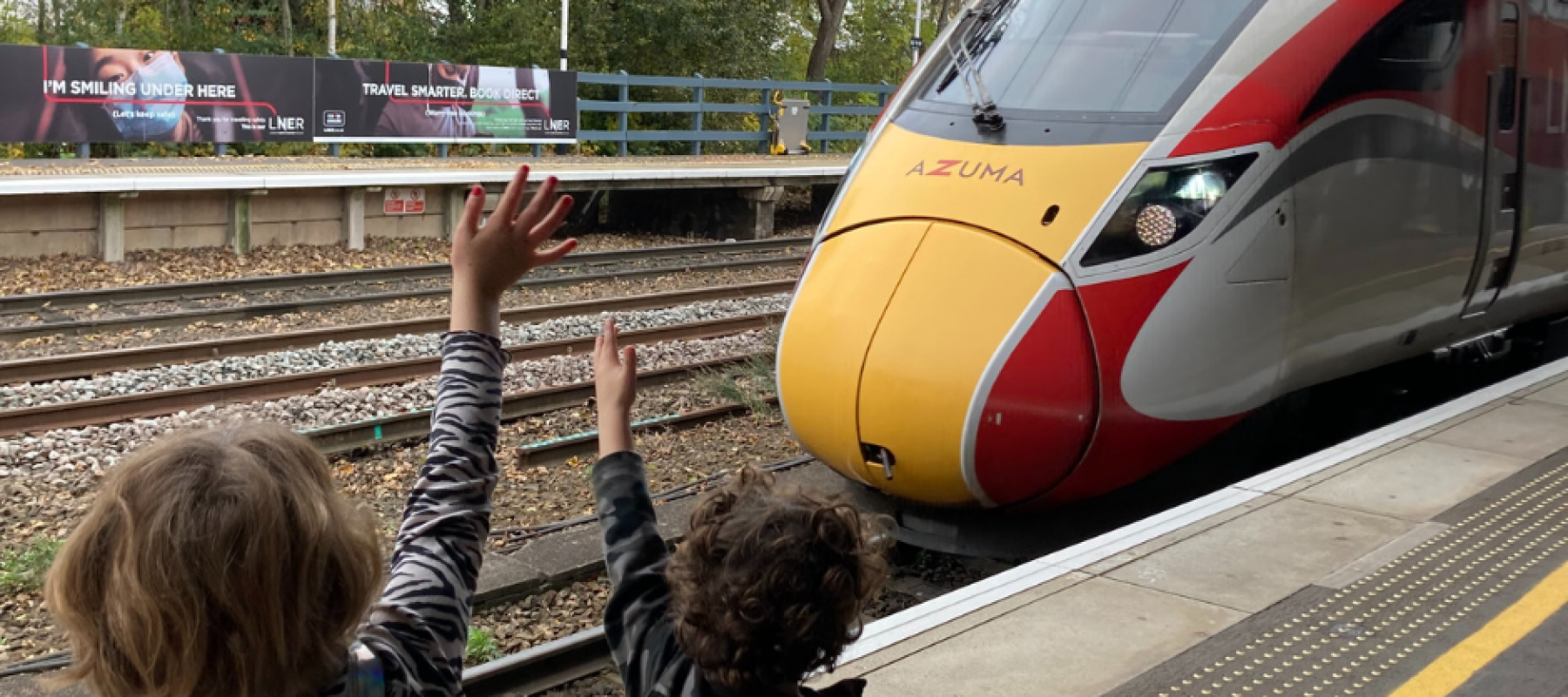 Family waving at train, before going on days out by rail