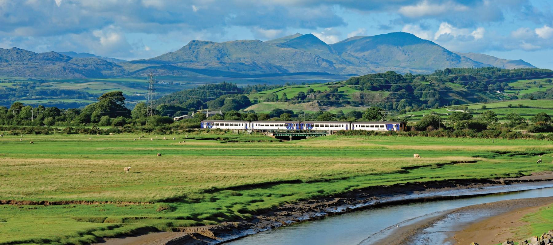 Train travelling through countryside with mountains in background