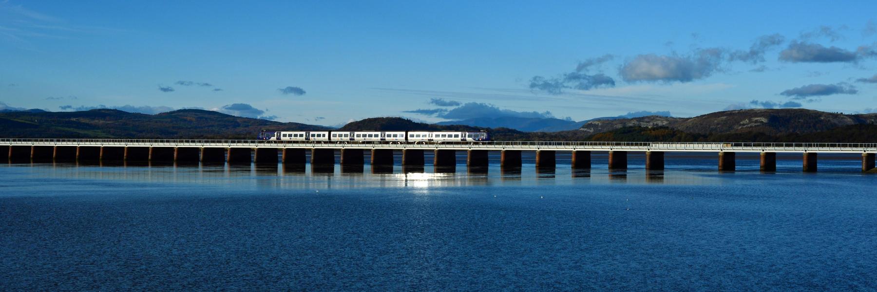 Train travelling across viaduct with Lake District mountain peaks in the distance